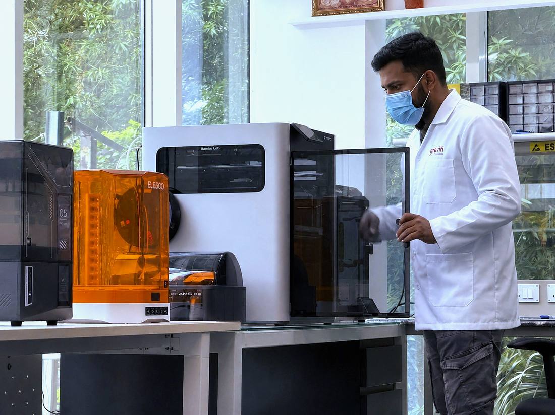 An engineer in a lab coat and respirator working at a bank of 3D printers in the Plazma hardware lab.