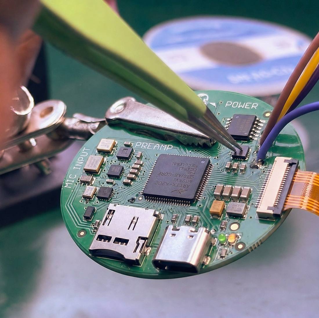 A hand soldering a component onto the round Plazma sensor board, its MIC INPUT, PREAMP and POWER sections labelled on the silkscreen.